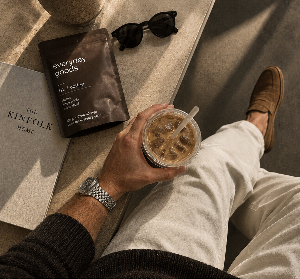 iced coffee held above cream corduroy trousers, with an everyday goods coffee pouch, sunglasses and a Kinfolk book on a stone ledge