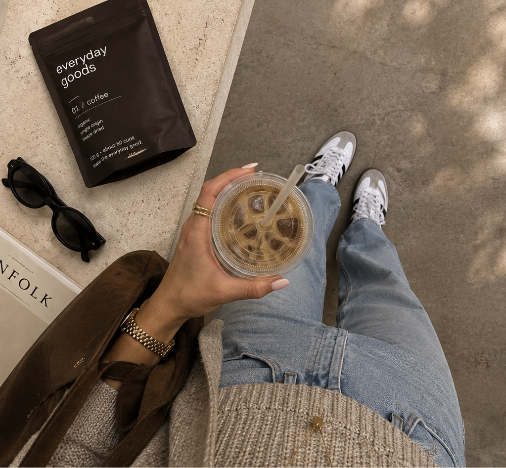 iced coffee held above vintage denim jeans and adidas sambas, with an everyday goods coffee pouch, sunglasses and a Kinfolk book on a stone ledge
