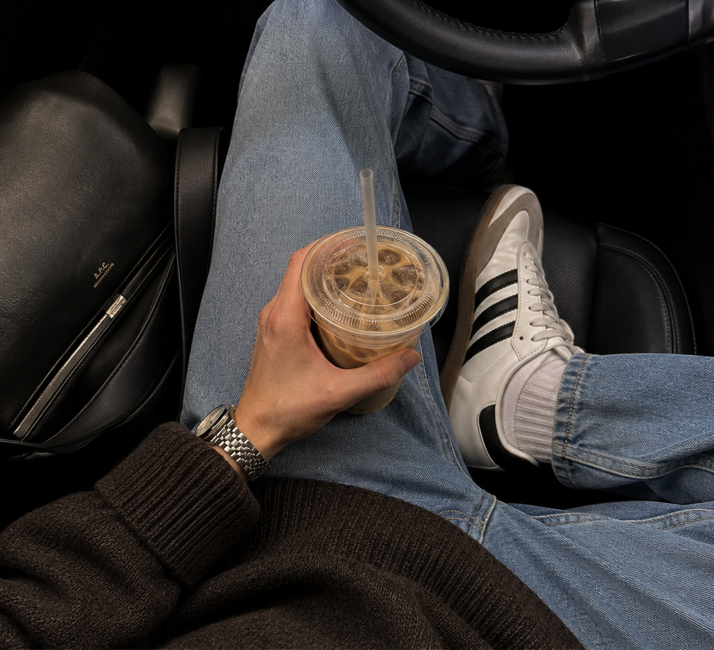 iced coffee held above denim jeans and adidas sambas in a car with black leather seats